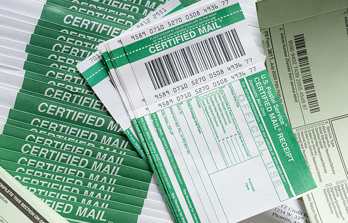 A tray of certified letters under a stack of certified mail forms and certified mail return receipt labels.